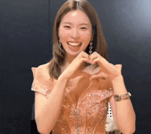 a woman in a pink dress is making a heart shape with her hands