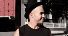 a man wearing a black hat and a black tank top is standing on a sidewalk .