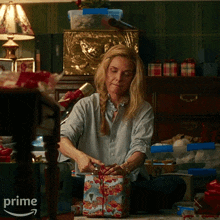 a woman sits on the floor wrapping a christmas present with an amazon prime logo behind her