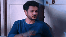 a man with a beard wearing a blue shirt is sitting in front of a door