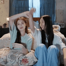 two women are sitting on a bed with their arms up