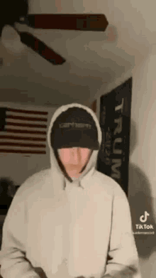 a man in a hoodie and hat is standing in front of a ceiling fan .