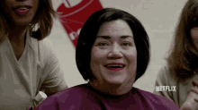 a woman with red lipstick is smiling while sitting in a barber shop .