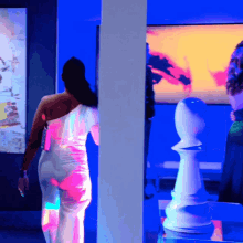 a woman in a white dress is standing in front of a chess piece
