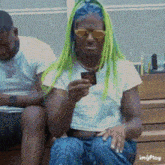 a woman with green hair is sitting on a bench holding a cup