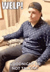 a man in a baseball cap is sitting on a couch and making a funny face .