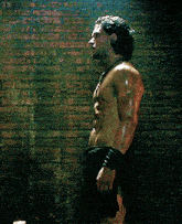 a shirtless man is standing in front of a brick wall with his arms outstretched