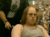a bald man wearing sunglasses is sitting in a chair in front of a man wearing a shirt that says ban the world