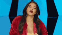 a woman wearing a red jacket and hoop earrings looks at the camera