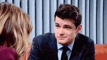 a man in a suit and tie is talking to a woman on a couch