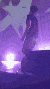 a man in a black shirt stands on a stage in front of a purple light