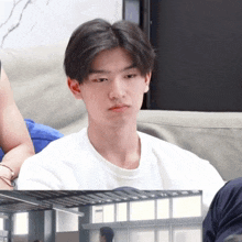 a man in a white shirt sits on a couch looking at the camera