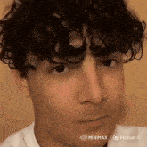 a young man with curly hair is wearing a white shirt .