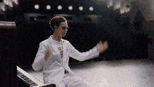 a man in a white suit sits at a piano