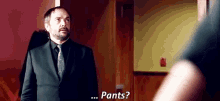 a man in a suit and tie is standing in front of a door and talking to another man .