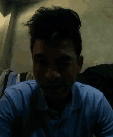 a man in a blue shirt is looking at the camera in the dark