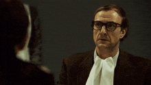 a man wearing glasses and a tie talks to a woman