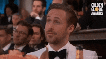 a man in a tuxedo and bow tie is sitting in a crowd of people at a golden globes awards .