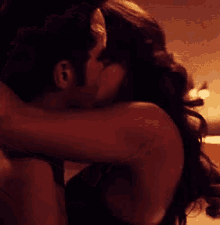 a man is holding a woman 's head in his arms in a dark room .