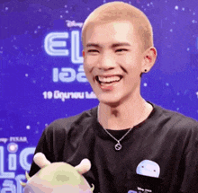 a young man is smiling while holding a stuffed animal in front of a sign that says el