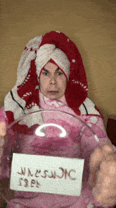 a man with a towel wrapped around his head is holding a glass bowl with a sign on it that says warning