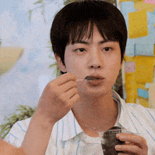 a young man is eating something with a spoon from a cup
