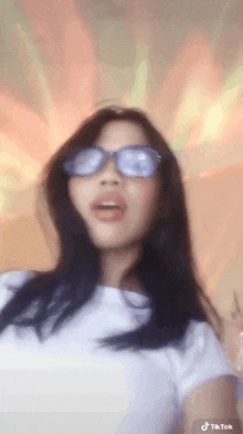 a woman wearing sunglasses and a white shirt is dancing .