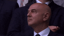 a bald man in a suit and tie is clapping his hands in a crowd .