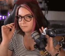 a woman wearing glasses is sitting in front of a microphone holding a controller .