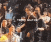 a man in a black suit is standing in a crowd of people and talking to another man .