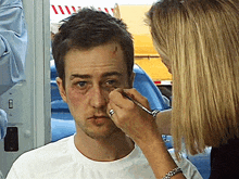 a woman is applying makeup to a man 's face with a brush