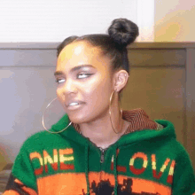 a woman wearing hoop earrings and a one love sweater