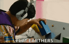a man wearing headphones looks at a blue box with the words flat earthers written on the bottom