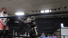 two wrestlers in a ring with one wearing a red headband and the other a black and gold outfit