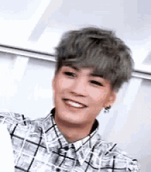 a young man with gray hair is smiling while wearing a plaid shirt .
