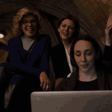 three women are sitting in front of a laptop and one of them is wearing a ring on her finger