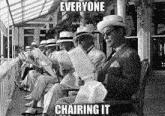 a black and white photo of a group of men reading newspapers with the caption " everyone chairing it "