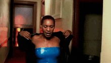a woman in a blue dress is taking off her jacket in a hallway .