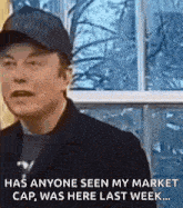 elon musk is wearing a baseball cap and talking to someone while standing in front of a window .