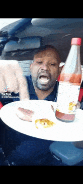 a man is holding a plate of food and a bottle of hot sauce
