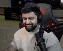 a man with a beard is sitting in front of a microphone wearing headphones and smiling .