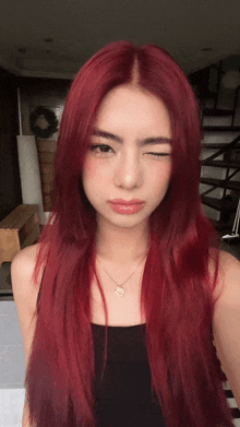 a woman with red hair and a black tank top winks