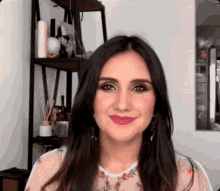 a woman with long dark hair is standing in front of a shelf and smiling at the camera .
