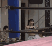 a woman in a bikini is standing in a boxing ring with her hands in the air