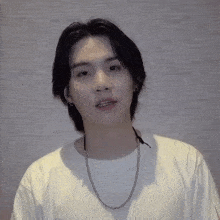 a young man wearing a white t-shirt and a necklace looks at the camera .