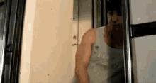 a man in a tank top is standing next to a refrigerator door .