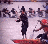 a young boy in a black hat stands on a red boat