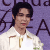 a man in a white jacket stands in front of a screen with the letter a visible