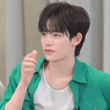 a young man wearing a green shirt and a white tank top is giving a thumbs up sign .