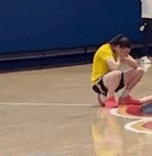 a person in a yellow shirt is squatting on a basketball court .
